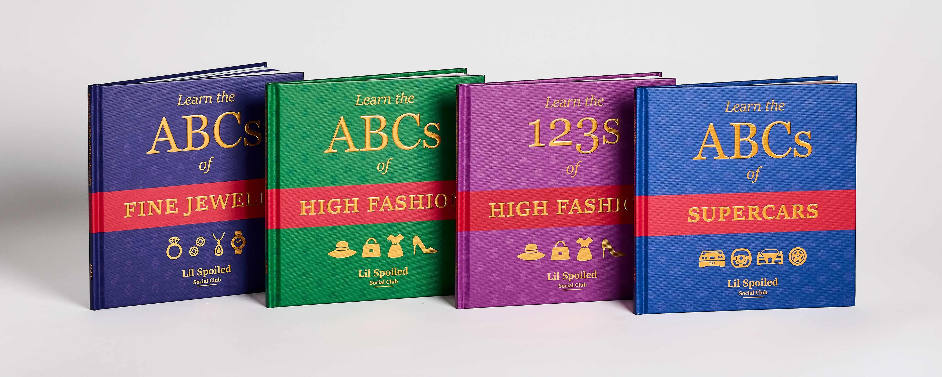 Four colorful books titled 'Learn the ABCs of Fine Jewelry', 'High Fashion', '123s of High Fashion', and 'Supercars' on a white background.