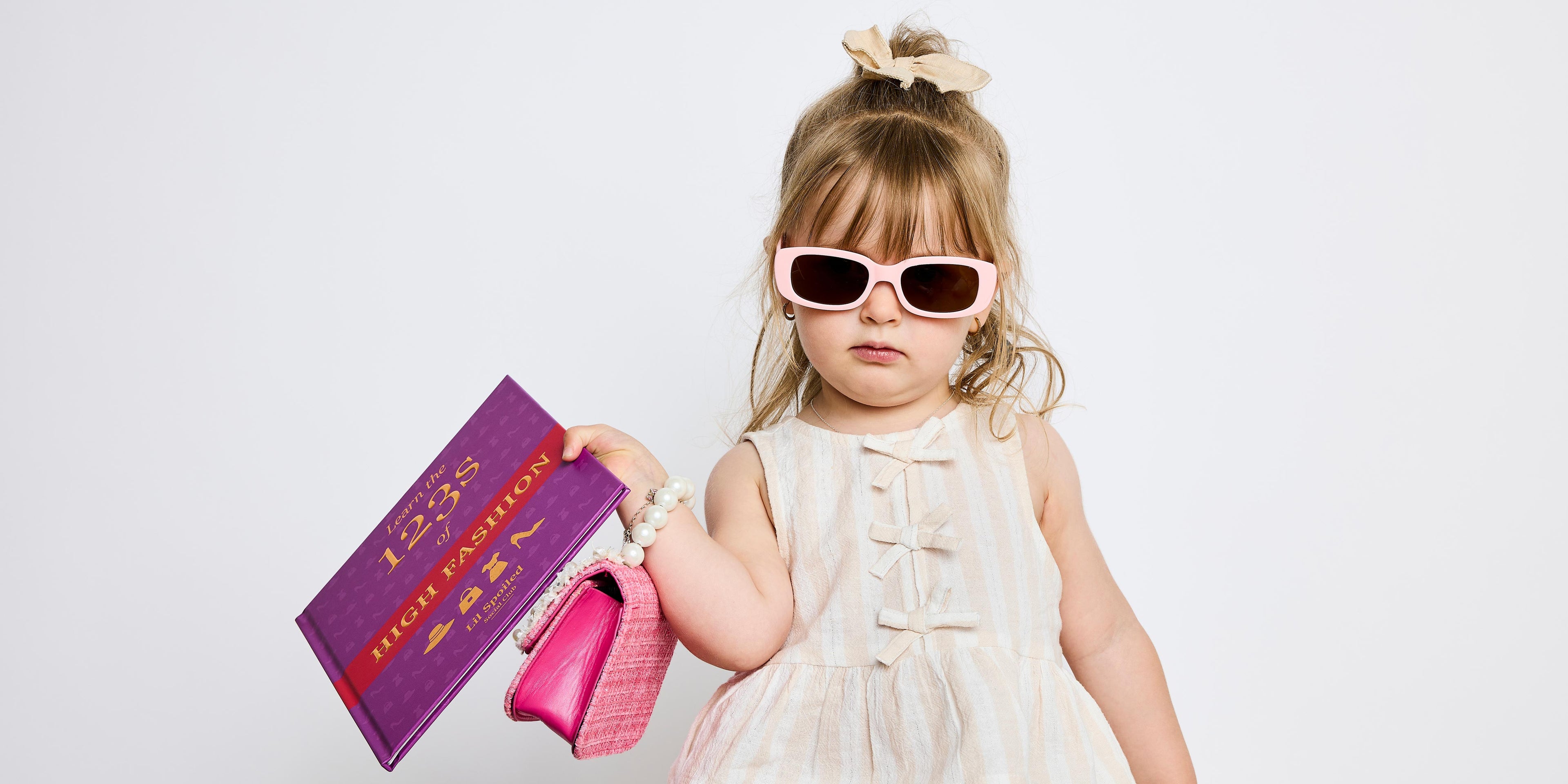 Young girl wearing sunglasses and holding a pink handbag and 'Learn the 123s of High Fashion' with a white background
