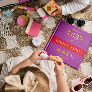 Child playing with toy makeup and books on a carpeted floor