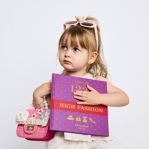 Young girl holding a book titled 'Learn the 123 High Fashion' with a pink purse on a white background