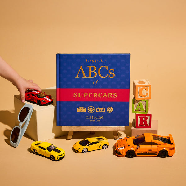 Book titled 'Learn the ABCs of Supercars' with toy cars and colorful blocks on a beige background