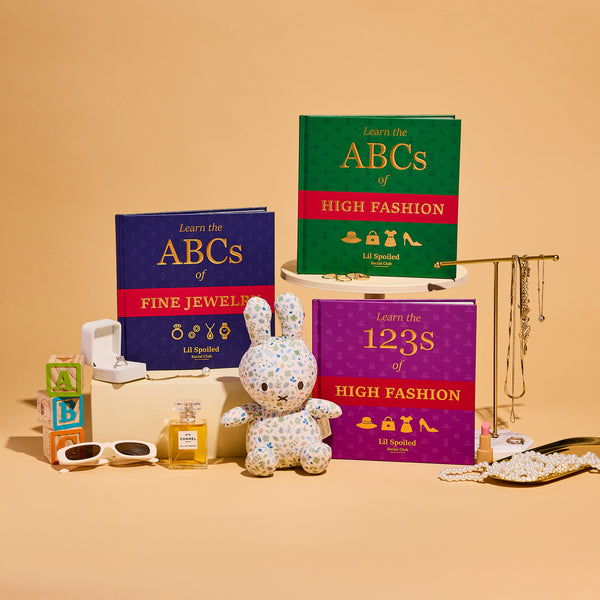 Educational books on fashion and jewelry with a decorative rabbit and accessories on a beige background. The books are Lil Spoiled Social Club ABCs and 123s books are displayed.