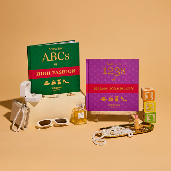 Two children's books titled 'Learn the ABCs of High Fashion' and 'Learn the 123s of High Fashion' on a beige background with fashion-themed accessories.