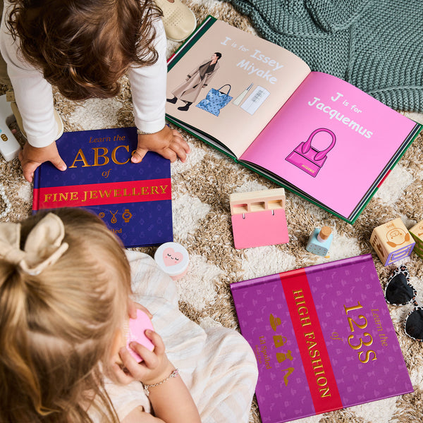 Two children playing with Lil Spoiled Social Club books on a carpeted floor.