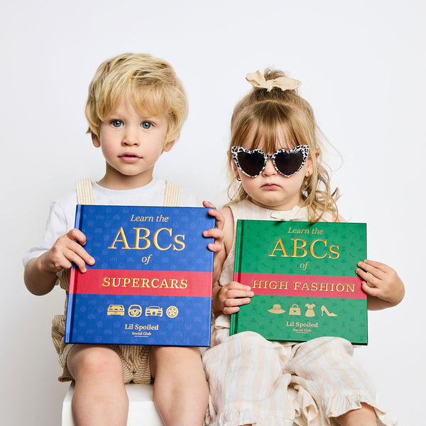 Two children holding books titled 'ABCs of Supercars' and 'ABCs of High Fashion' against a white background.