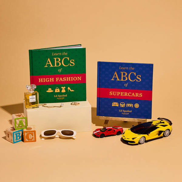 Two books titled 'ABCs of High Fashion' and 'ABCs of Supercars' with toy cars and accessories on a beige background.